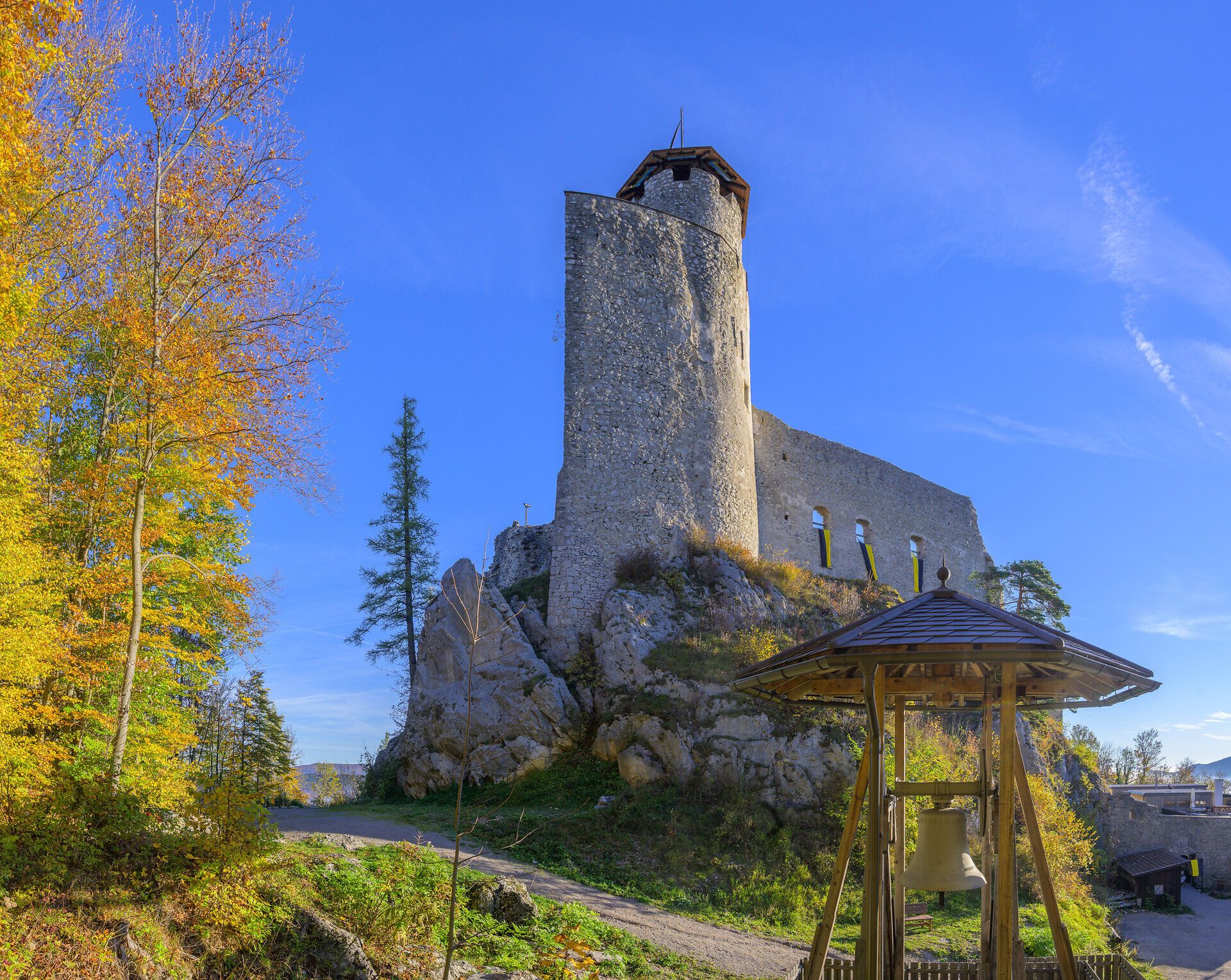 Araburg bei Kaumberg thront auf einem bewaldeten Hügel an einem klaren Herbsttag; über der Ruine spannt sich ein tiefblauer Himmel, während gelb‑orange verfärbte Laubbäume die Araburg umgeben.