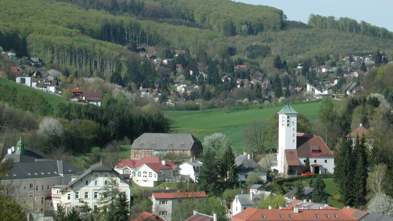 Panorama von Gablitz mit Kirche und umliegenden Häusern vor bewaldeten Hügeln.