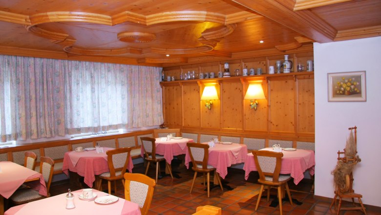 Gemütlicher Frühstücksraum mit Holzmöbeln, rosa Tischdecken und dekorativen Krügen auf einem Regal.