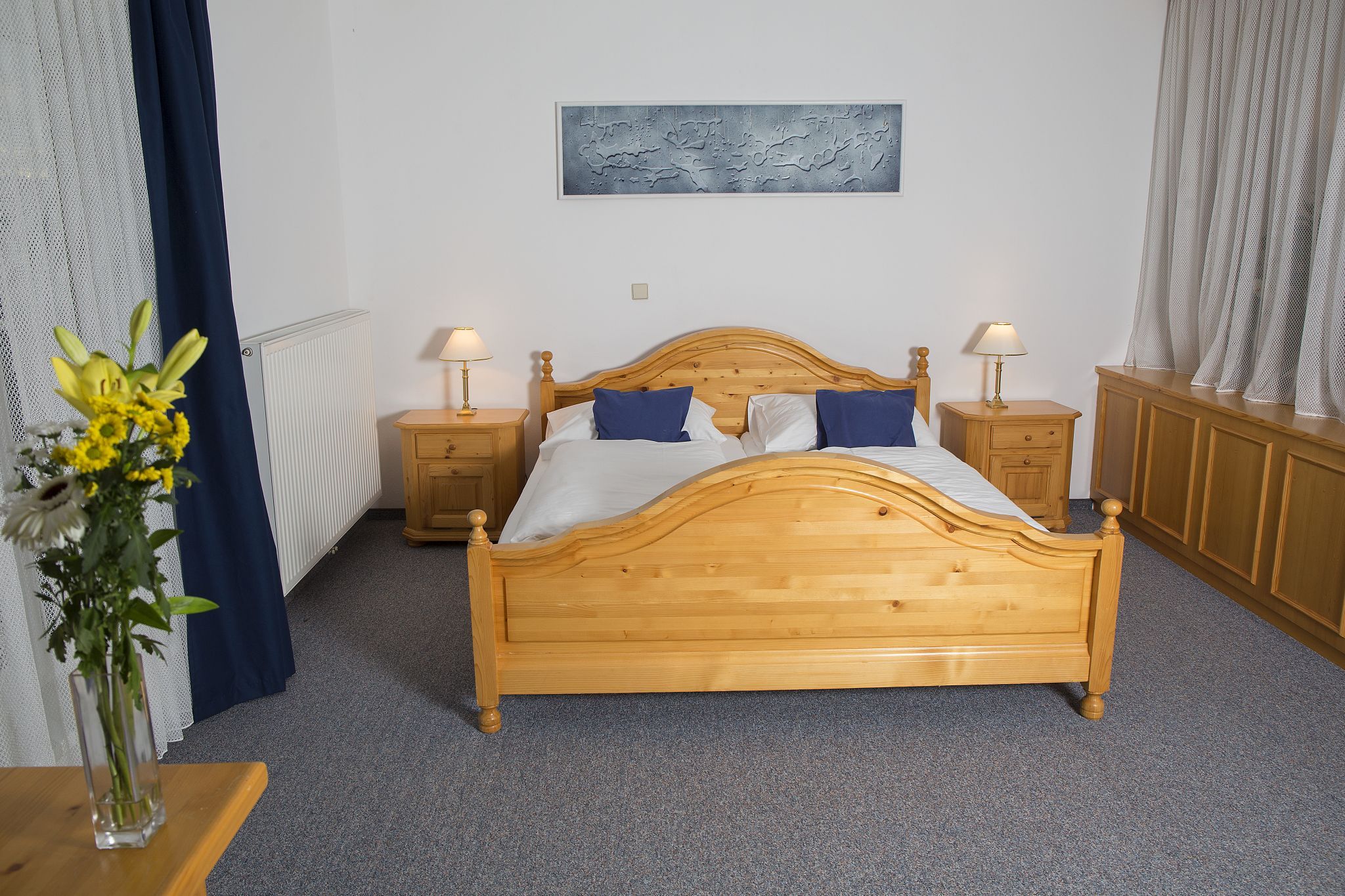 Ein Schlafzimmer mit einem Doppelbett aus Holz, zwei Nachttischen mit Lampen und einem Blumenstrauß auf einem Tisch.