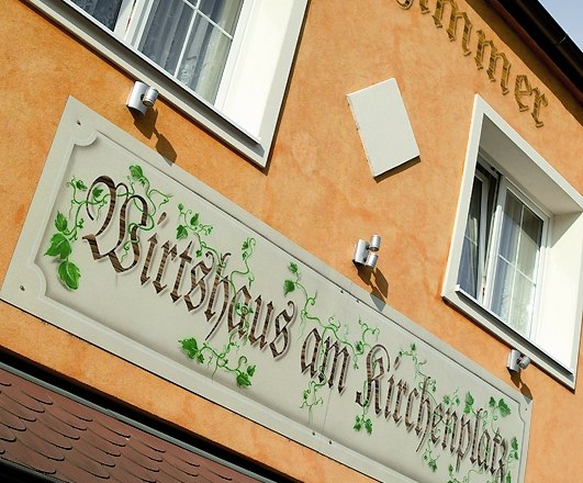 Facade of a building with the sign 'Wirtshaus am Kirchenplatz'.
