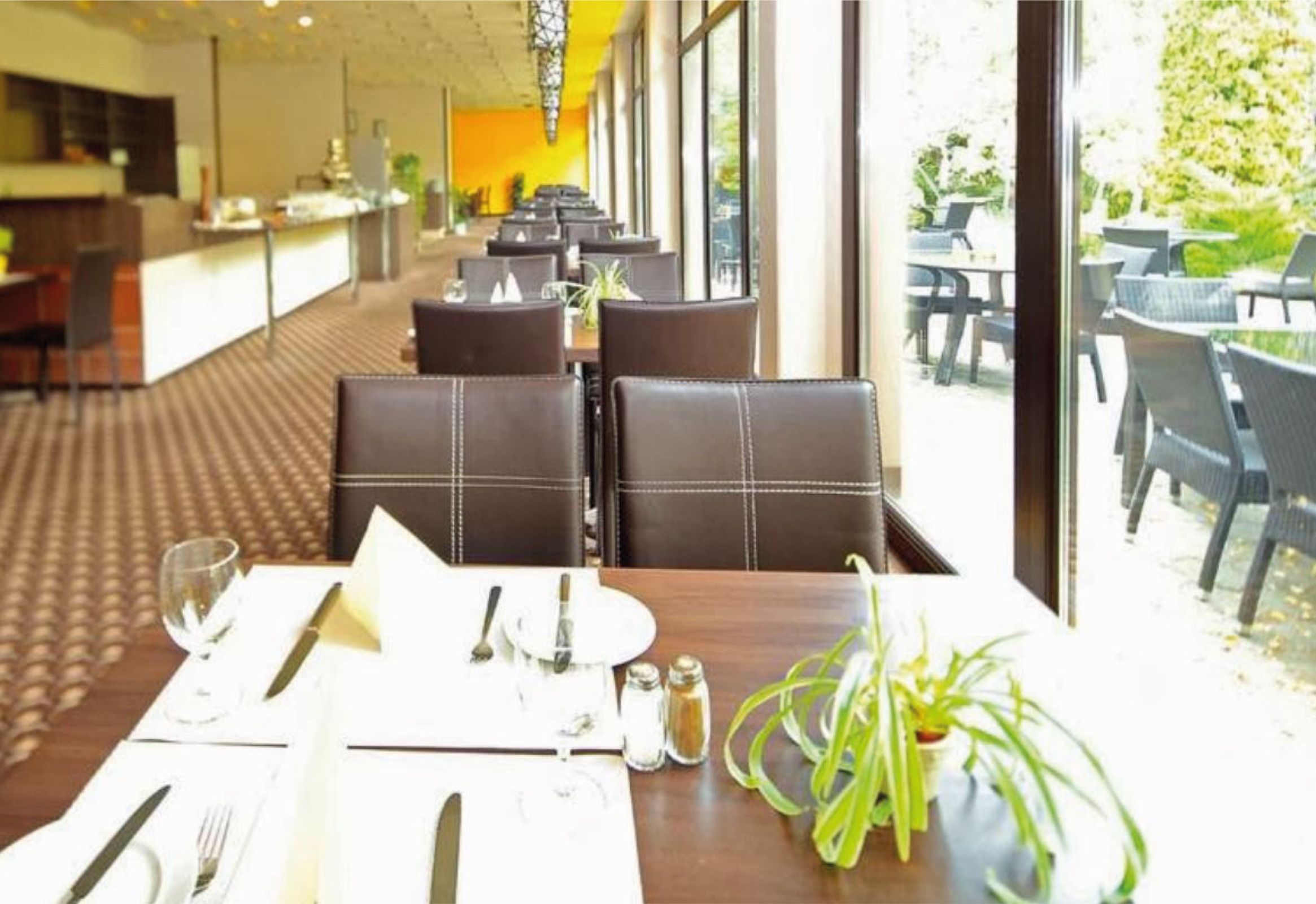 Innenansicht eines Restaurants mit gedeckten Tischen und großen Fenstern.