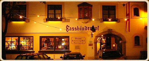 Nachtaufnahme eines Geb&auml;udes mit der Aufschrift 'Fassbinderhof', beleuchtet von Lichterketten.