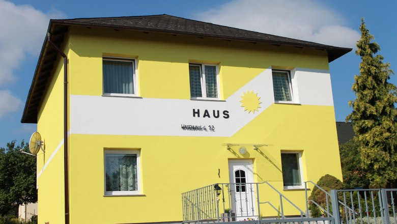 Eingang Haus Sonne, © privat Gelbes Haus mit der Aufschrift 'Haus' und einer Sonne auf der Fassade.
