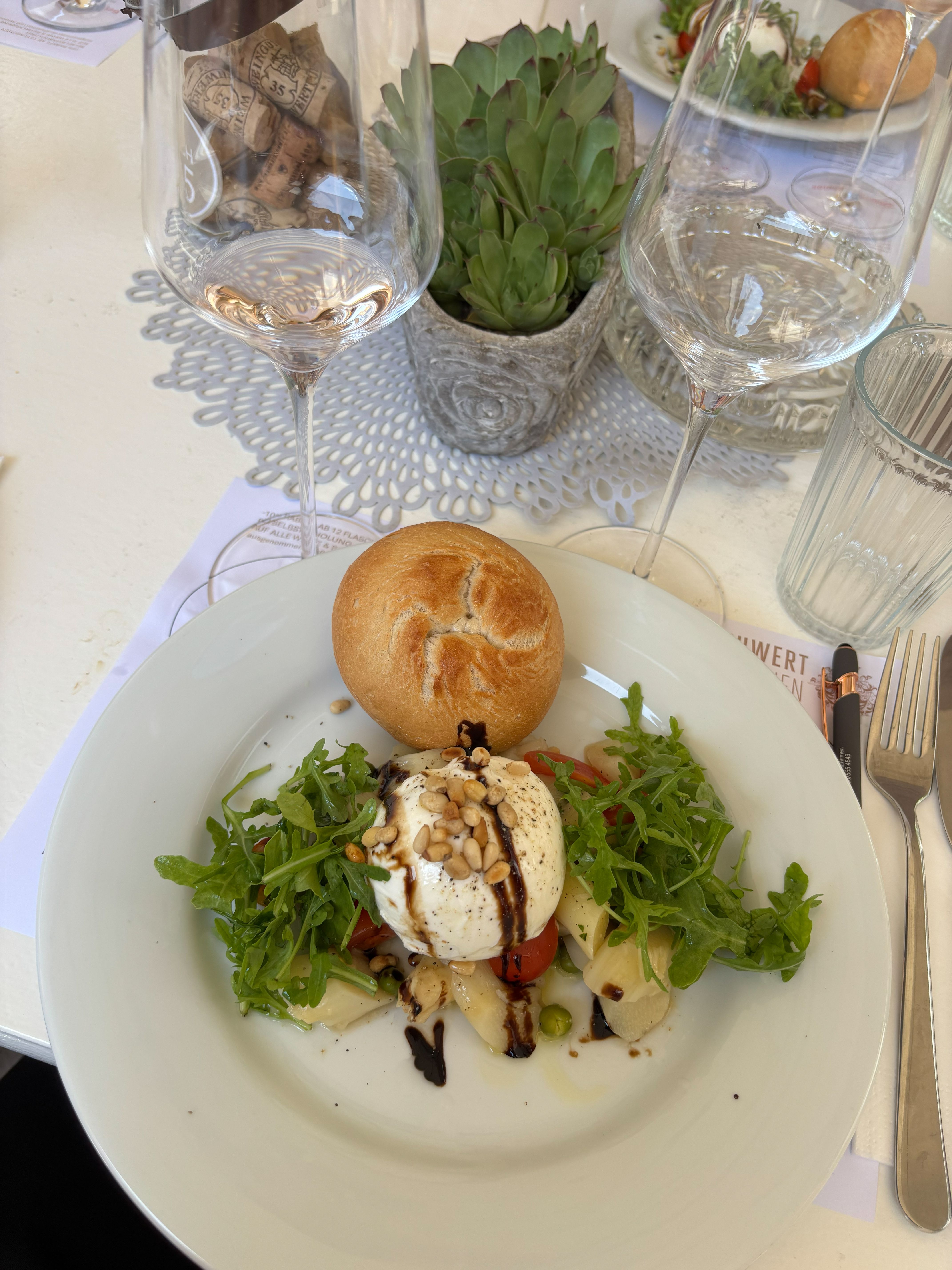 Vorspeise bestehend aus Mozzarella, Tomaten und Rucola, dazu serviert eine Semmel und Weingläser.