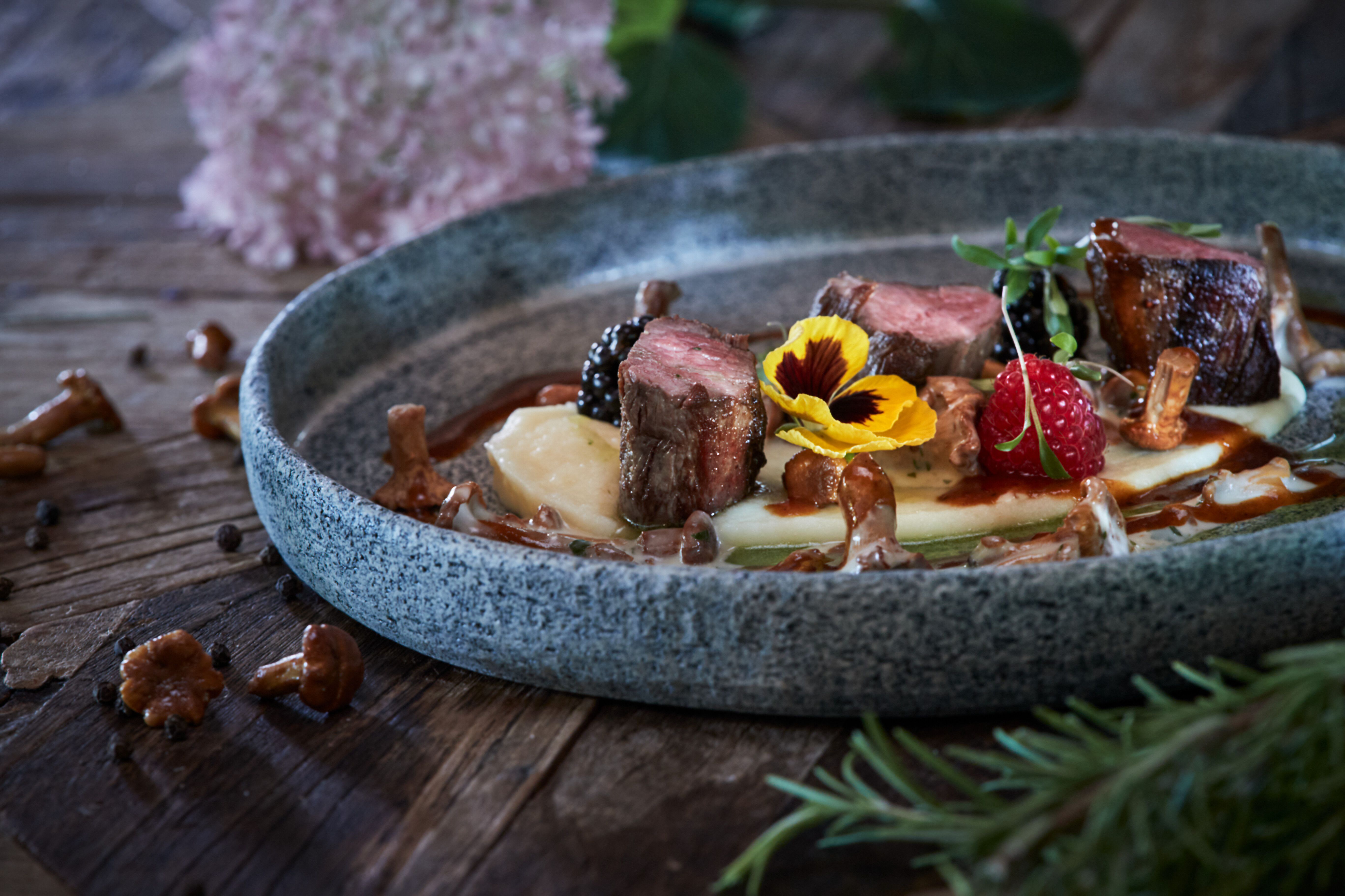 Ein köstliches Rehfilet, perfekt zubereitet und garniert mit frischen Eierschwammerln, lädt zu einem genussvollen Erlebnis ein. Die liebevolle Präsentation auf dem rustikalen Teller verspricht ein Fest für die Sinne, während die umgebende Natur des Wienerwaldes eine einladende Atmosphäre schafft.