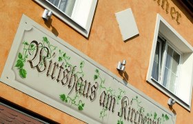 Fassade eines Gebäudes mit dem Schild 'Wirtshaus am Kirchenplatz'.