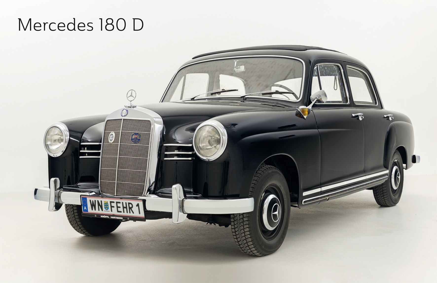 Ein schwarzer Mercedes 180 D Oldtimer in einem Studio mit weißem Hintergrund.