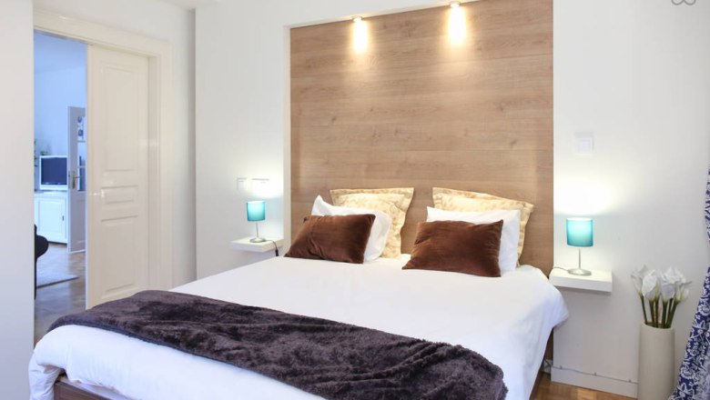 Modernes Schlafzimmer mit Doppelbett, Holzrückwand und blauen Nachttischlampen.