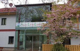 Eingang des Smart Liv'in Laabnerhof mit blühendem Baum.
