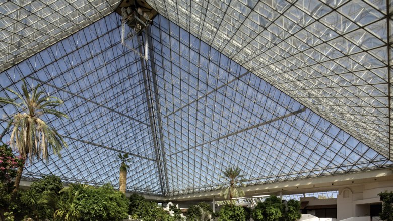 Event pyramid, © Eventhotel Pyramide GmbH Interior view of a large glass pyramid with plants and palm trees.