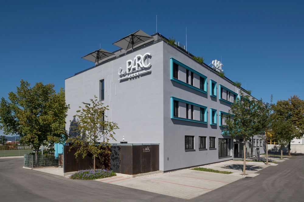Modernes Gebäude mit der Aufschrift 'Le Parc' und Bäumen im Vordergrund.