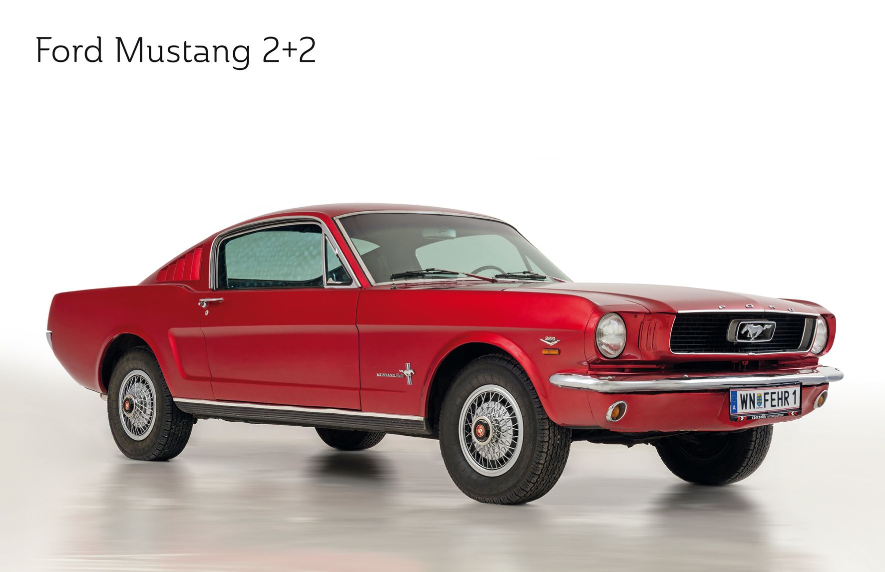 Ein roter Ford Mustang 2+2 aus den 1960er Jahren, seitlich fotografiert auf weißem Hintergrund.