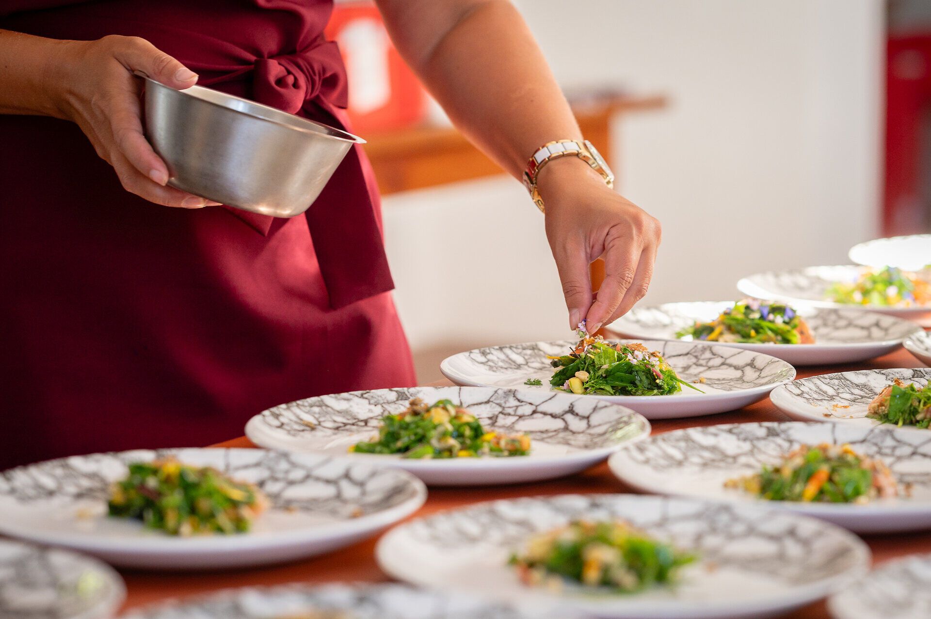 Ein Tisch gedeckt mit mehreren weiß gemusterten Porzellantellern, auf denen sich liebevoll angerichtete Seeforellen befinden. Die Fische sind mit Douglasie gebeizt und werden von einer frischen Wildkräuter-Salsa akzentuiert.