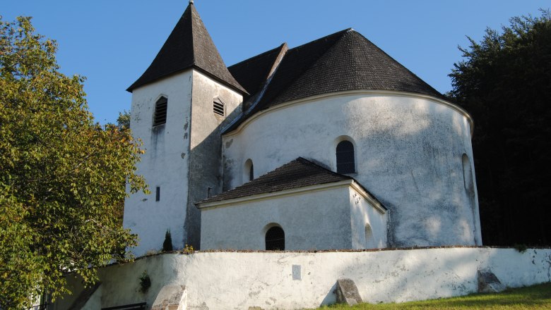 Weiße Kirche mit Turm und abgerundetem Dach, umgeben von Bäumen.