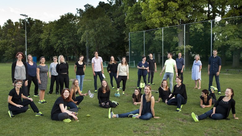 A group of people pose smiling in a meadow, surrounded by trees and a fence.