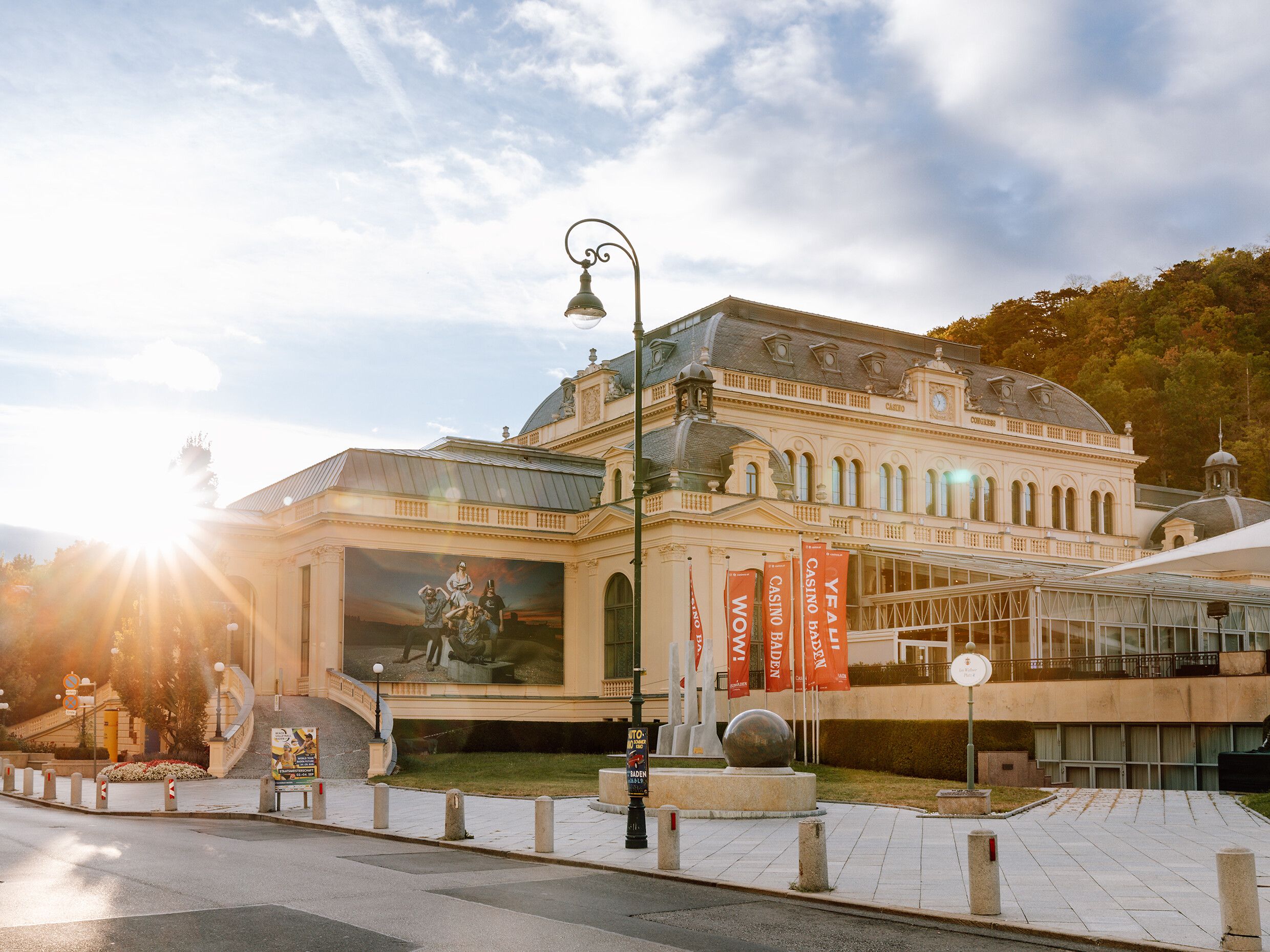 Die goldenen Strahlen der Abendsonne umspielen die prächtige Fassade des Casinos, während die umliegenden Bäume sanft im Wind wiegen. Ein Ort, der die Seele mit seiner eleganten Architektur und der ruhigen Atmosphäre verzaubert, lädt dazu ein, die Schönheit des Sommers im Wienerwald zu genießen.