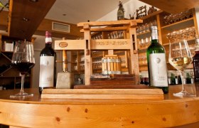 Wine bottles and glasses next to a small wooden press on a counter.
