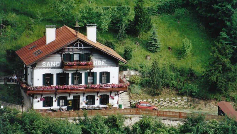 Traditionelles Haus namens Sand-Hof in gr&uuml;ner Landschaft.