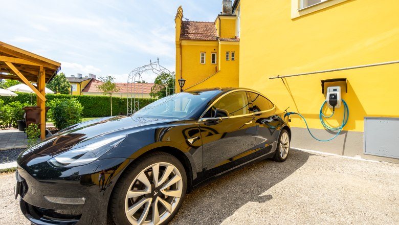 Schwarzes Elektroauto lädt an gelber Hauswand.