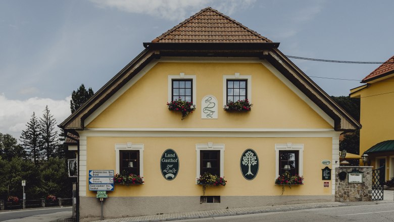 Gelbes Gasthaus mit Blumenkästen und Schildern an der Fassade.