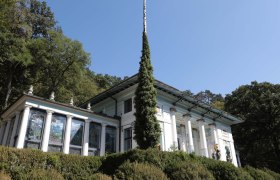 Ernst Fuchs Museum with columns and stained glass windows, surrounded by trees.