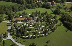 Luftaufnahme eines Campingplatzes inmitten grüner Landschaft mit Wohnwagen und Zelten.