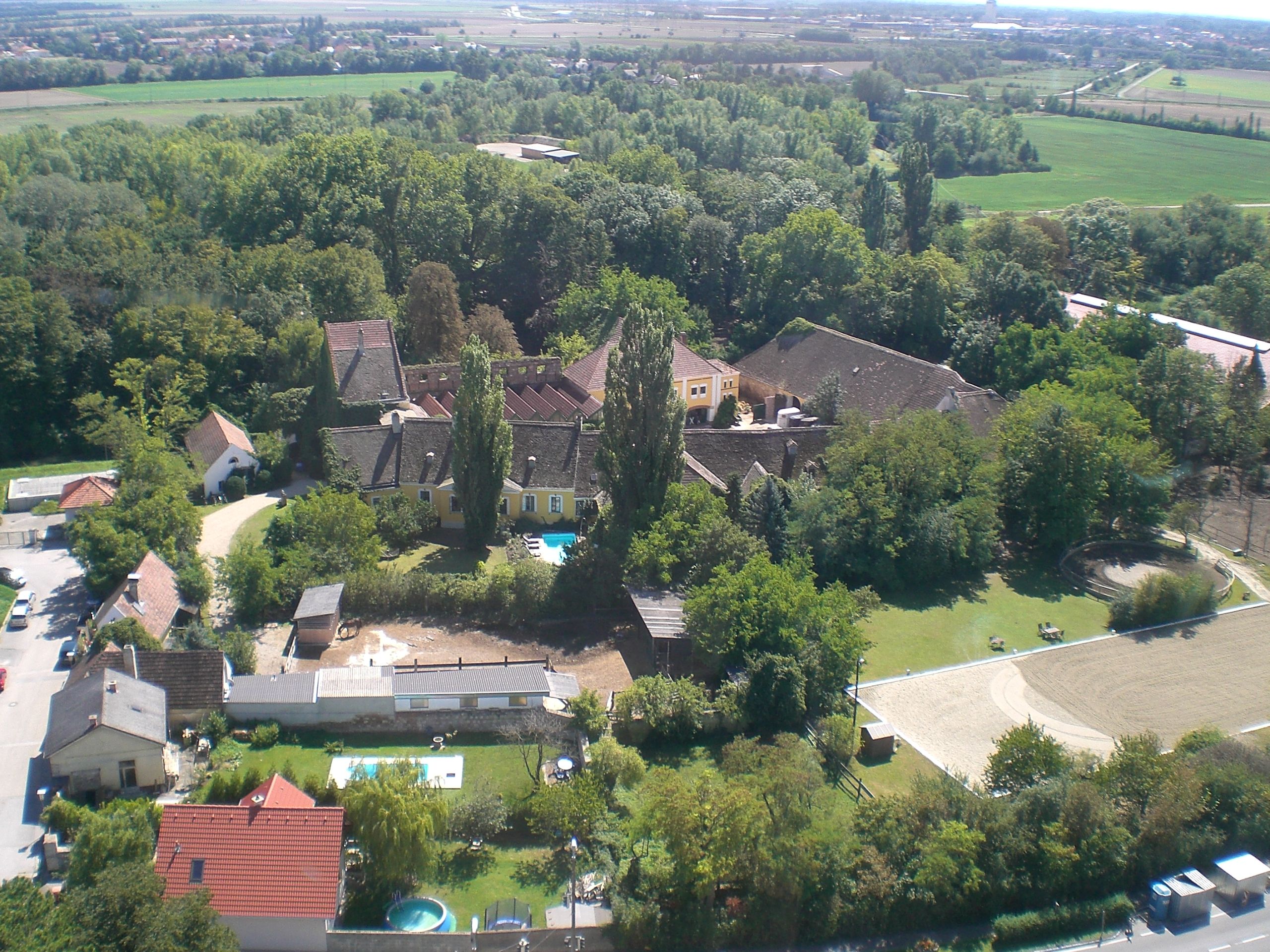Luftaufnahme eines Reitstalls mit Gebäuden, Bäumen und Reitplatz.