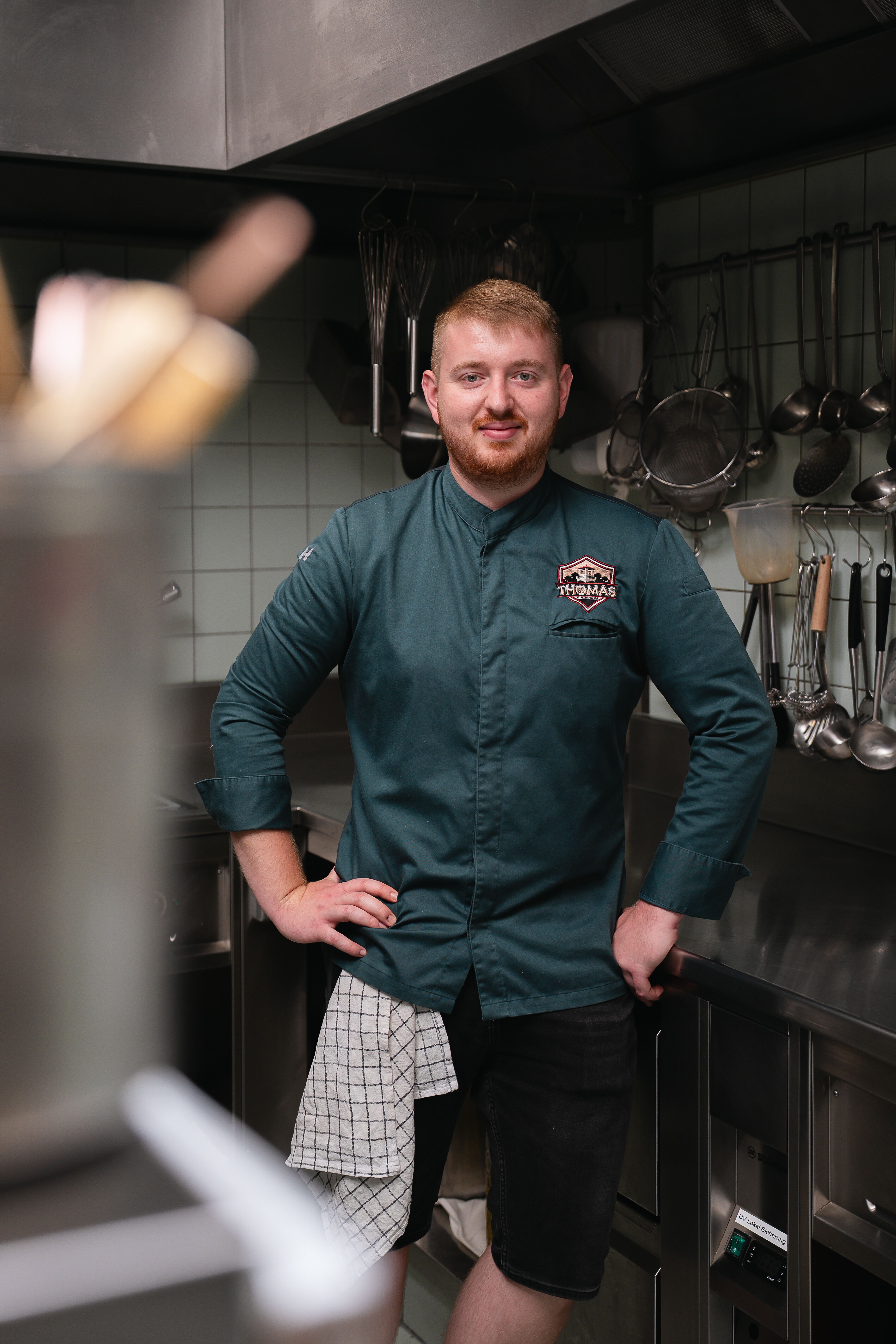 Thomas Reinisch steht in der Küche im Lokal Thomas im Johanneshof, blickt in die Kamera, Arme an die Hüfte gelehnt.