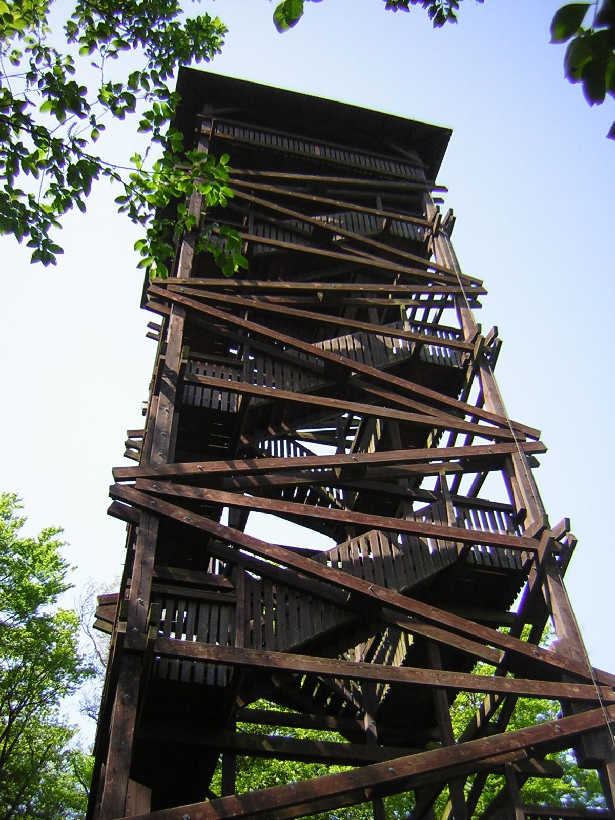 Holzturm mit Treppen und Geländern, umgeben von Bäumen.