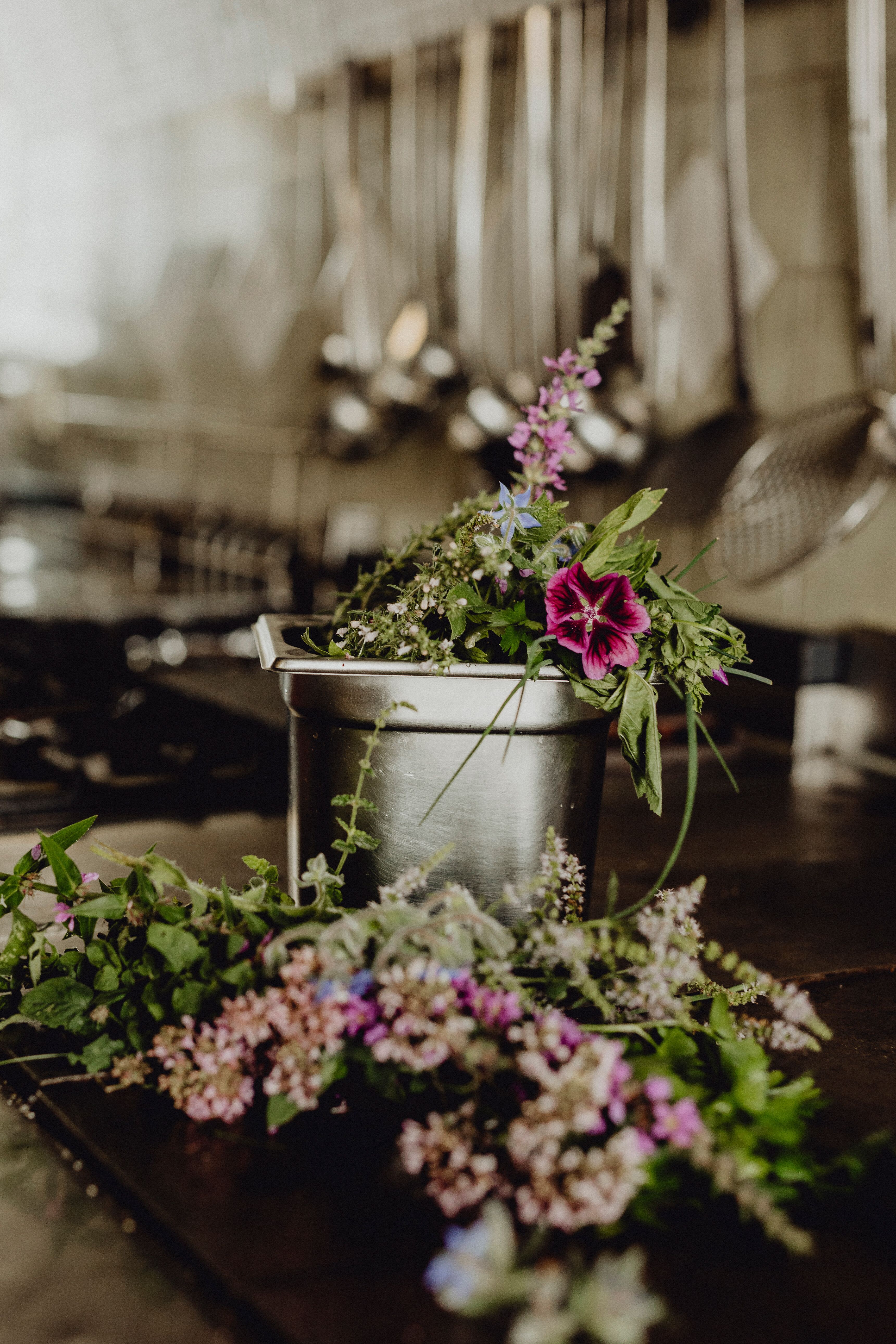 Ein rustikales Ambiente wird durch die frischen Blumen in einem Eimer unterstrichen, die den Raum mit lebendigen Farben füllen. Die Kombination aus Natur und traditioneller Wirtshauskultur schafft eine einladende Atmosphäre, die zum Verweilen einlädt.