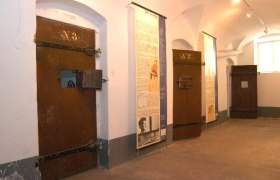 Three prison doors in a corridor with information boards on the walls.