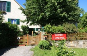 Ein Haus mit Garten und einem Schild "Pension Lindenhof" am Holzzaun.