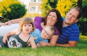 Eine Familie liegt l&auml;chelnd auf einer Wiese, bestehend aus zwei Erwachsenen und zwei Kindern.