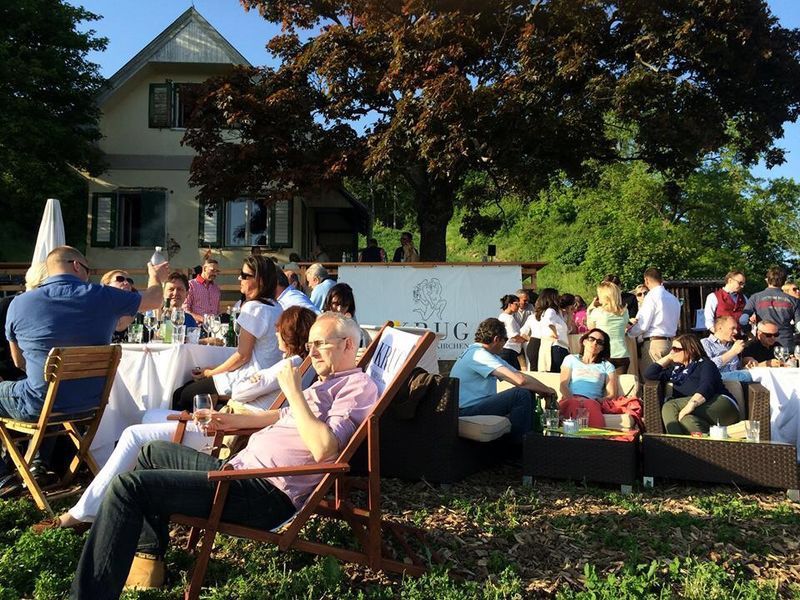 Menschen entspannen bei einer Gartenparty vor einem Haus mit Bäumen.
