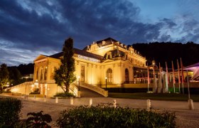 Beleuchtetes Casino Baden bei Nacht mit dramatischem Himmel.