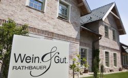 Ein Schild mit der Aufschrift 'Wein & Gut Rathbauer' vor einem Backsteingebäude.