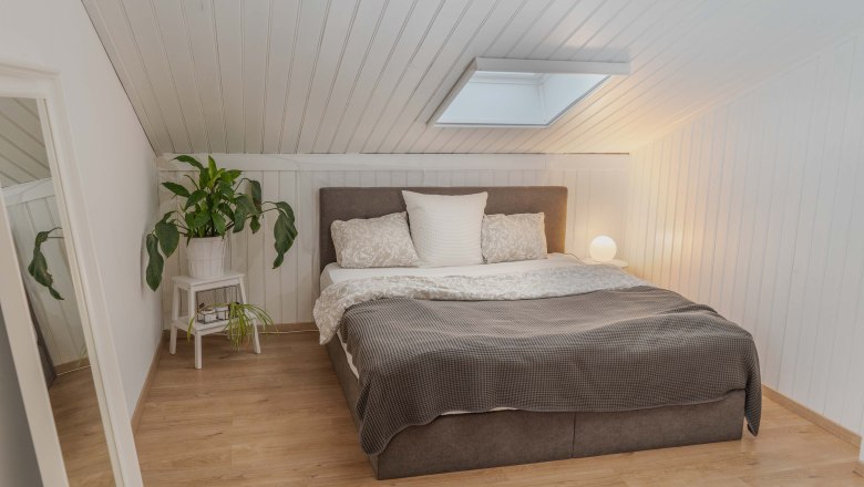 Gemütliches Schlafzimmer mit Dachschräge, Bett, Pflanzen und Lampe.