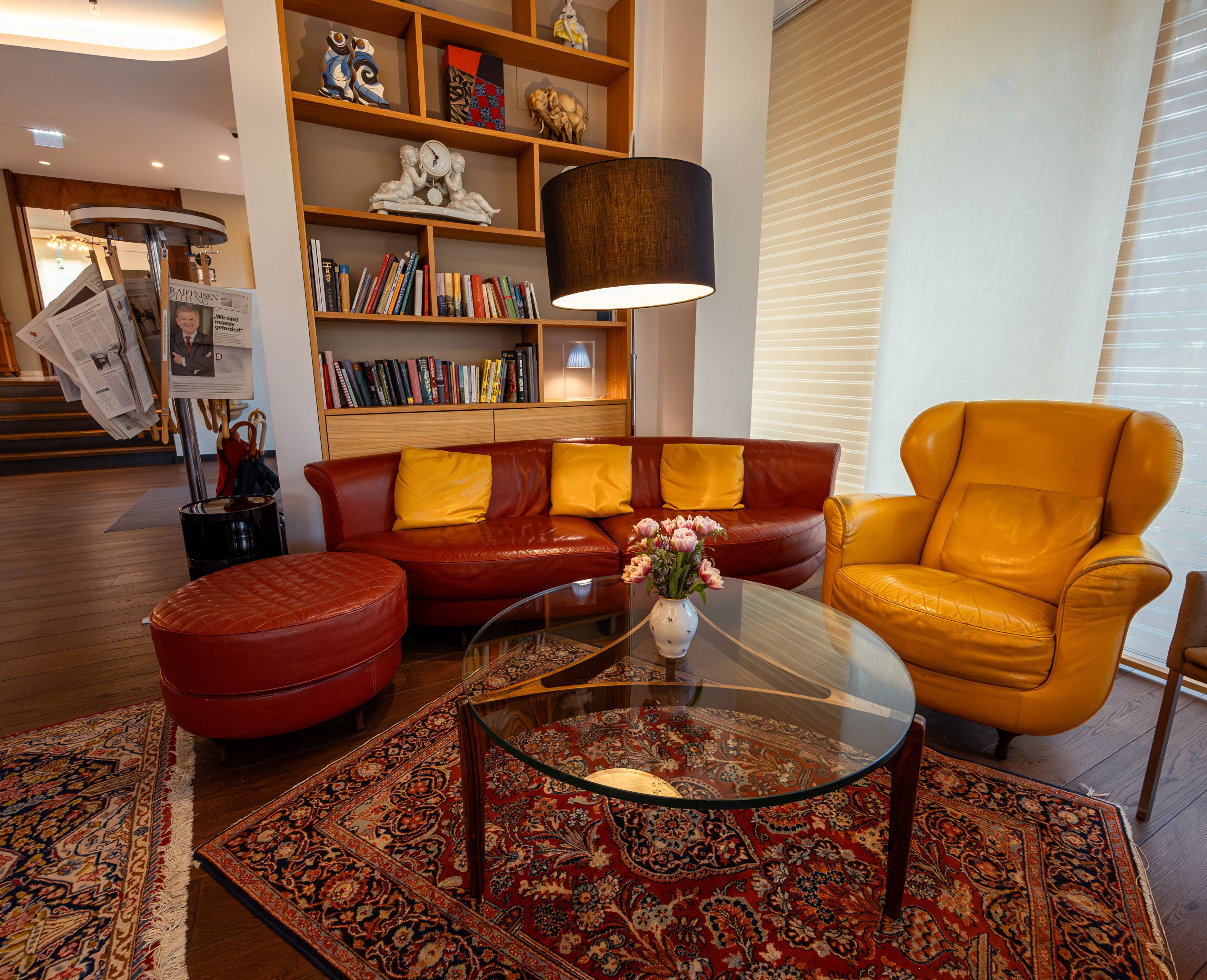 Gemütliche Hotellobby mit roten und gelben Ledermöbeln, Bücherregal und Zeitungsständer.