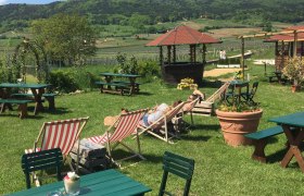 Garten mit Liegest&uuml;hlen und Tischen, im Hintergrund H&uuml;gel und blauer Himmel.
