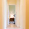 A bright hallway leads to a bedroom with bedside lamp.
