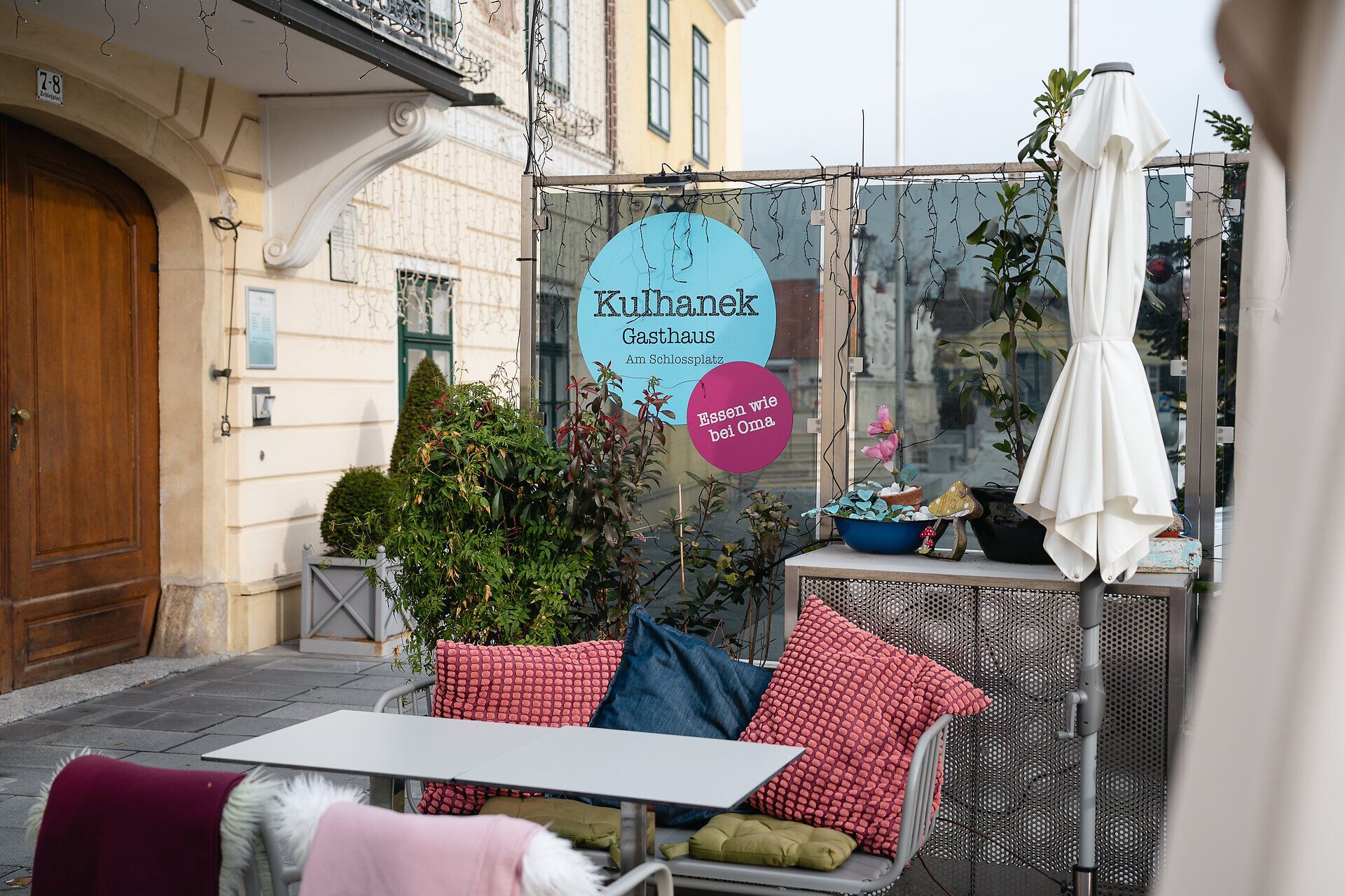 Gleich beim Betreten von Kulhaneks Gastgarten auf dem Schlossplatz entfaltet sich ein zauberhaftes Bild. Gemütlich mit bunten Decken dekorierte Stühle laden zum Verweilen ein und schaffen eine warme Atmosphäre, perfekt für einen kühleren Herbsttag. Die Farben der Decken spiegeln die herbstliche Umgebung und erzeugen ein harmonisches Zusammenspiel, das einladend wirkt. Hier, in dieser Oase der Behaglichkeit, fühlt man sich willkommen und kann entspannt verweilen.