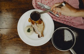 A plate of caraway roast and potato dumplings, covered in gravy, on a wooden table.