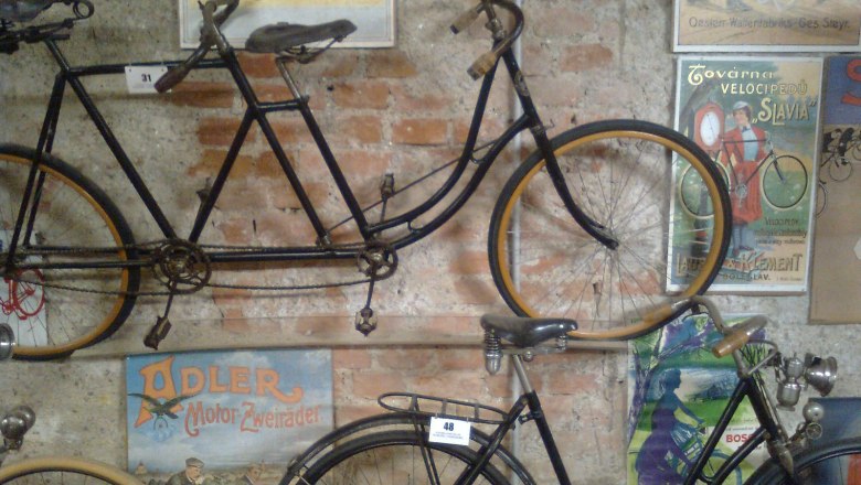 Alte Fahrräder und Vintage-Poster an einer Backsteinwand im Fahrradmuseum Schloss Vösendorf.