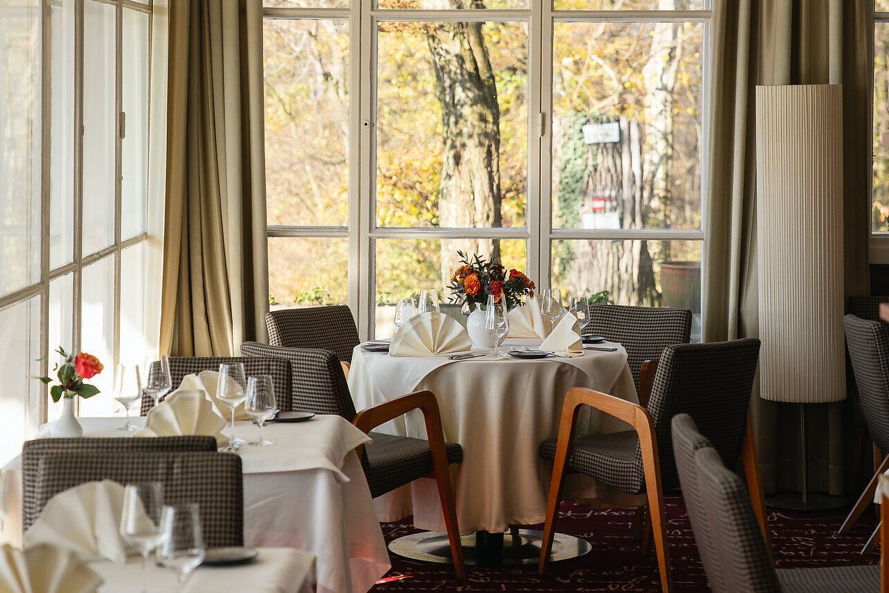 Ein elegant gedeckter Restaurantbereich im Berghotel Tulbingerkogel. Der Raum wird von hellem Licht durchflutet und bietet einen malerischen Blick auf die herbstlichen Bäume draußen, welche in warmen Farben leuchten.