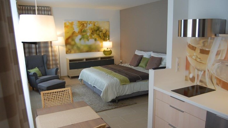 Modernes Apartment mit Bett, Sessel, Tisch und Küchenzeile.
