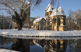 Winterliche Schlossruine Pottendorf mit Schnee und Spiegelung im Wasser.