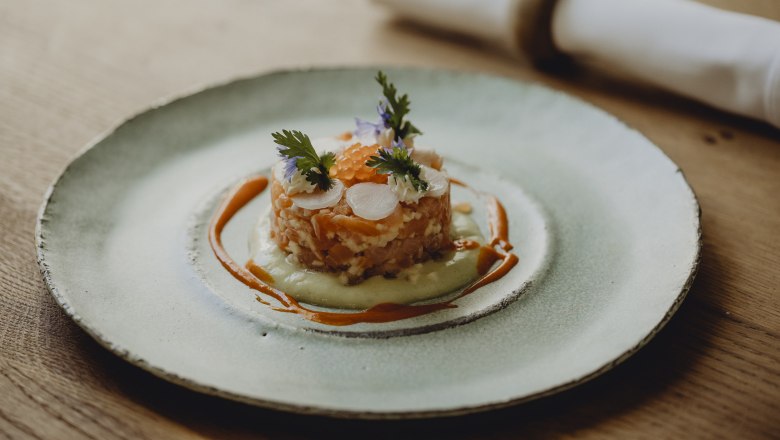 Gourmetgericht auf einem Teller mit Lachs, Kräutern und Soße dekoriert.
