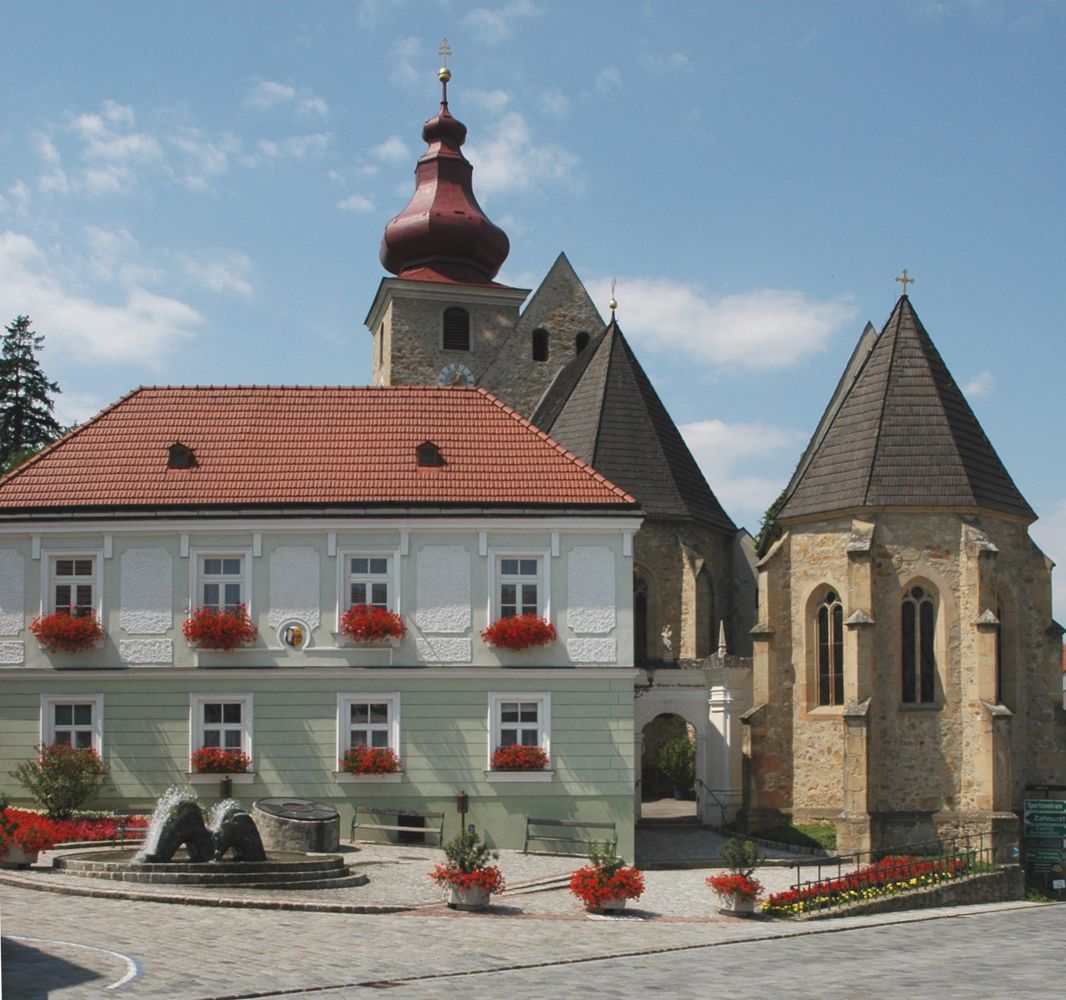Historisches Gebäude mit rotem Dach und Kirche im Hintergrund auf dem Marktplatz Maria-Anzbach.