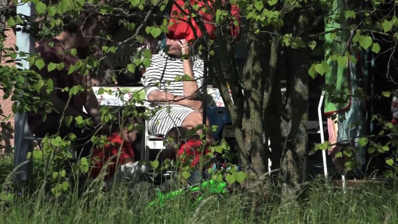 People sit in the shade under a tree, partially hidden by leaves.